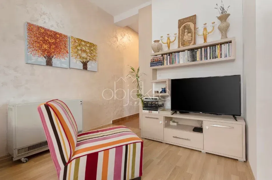 Dnevni boravak sa foteljom, TV-om, policom za knjige i slikama na zidu.