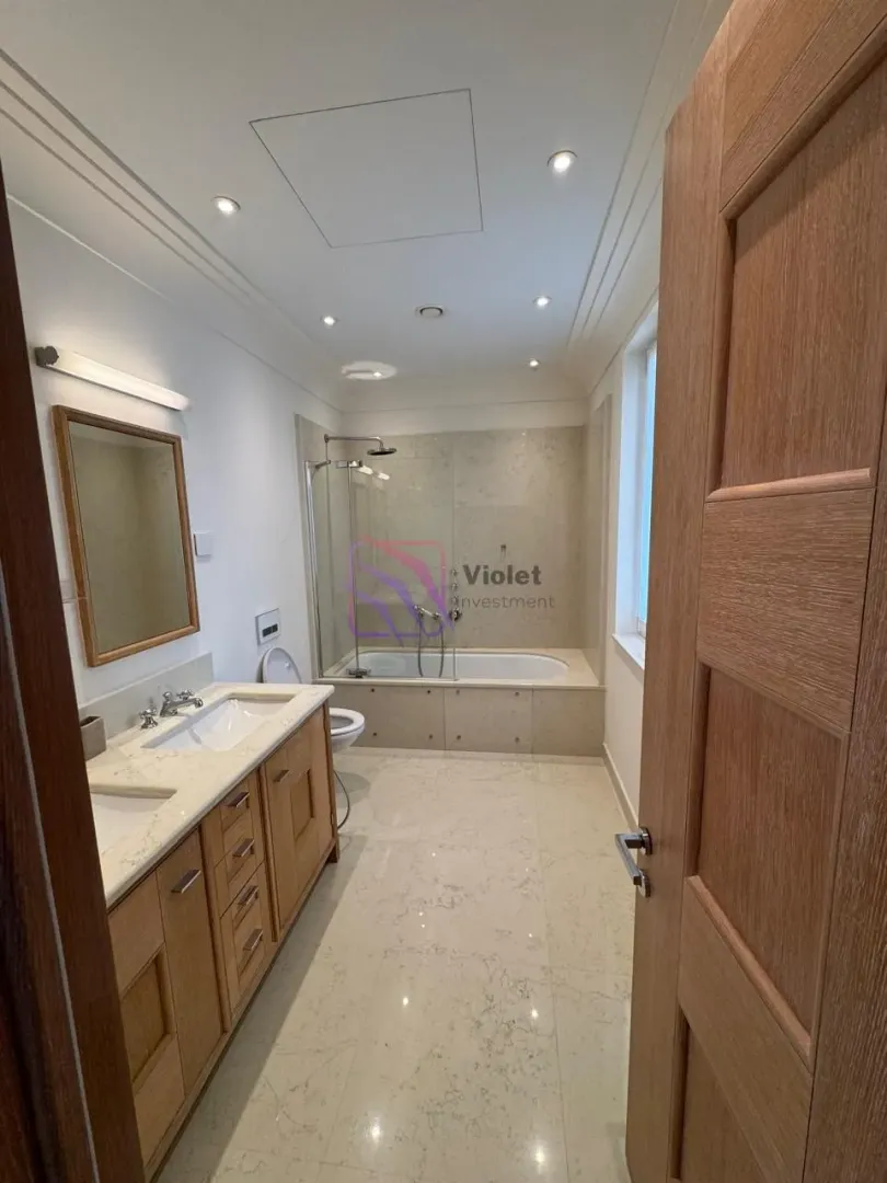 Spacious bathroom with a wooden vanity, double sinks, a bathtub, and a glass shower partition.