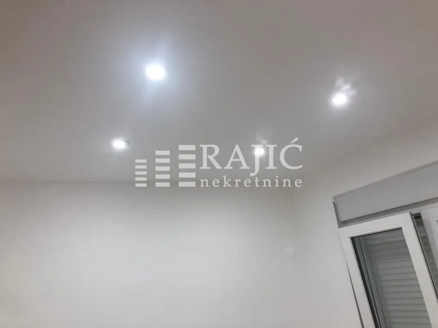 View of a white ceiling with recessed lighting and part of a window.