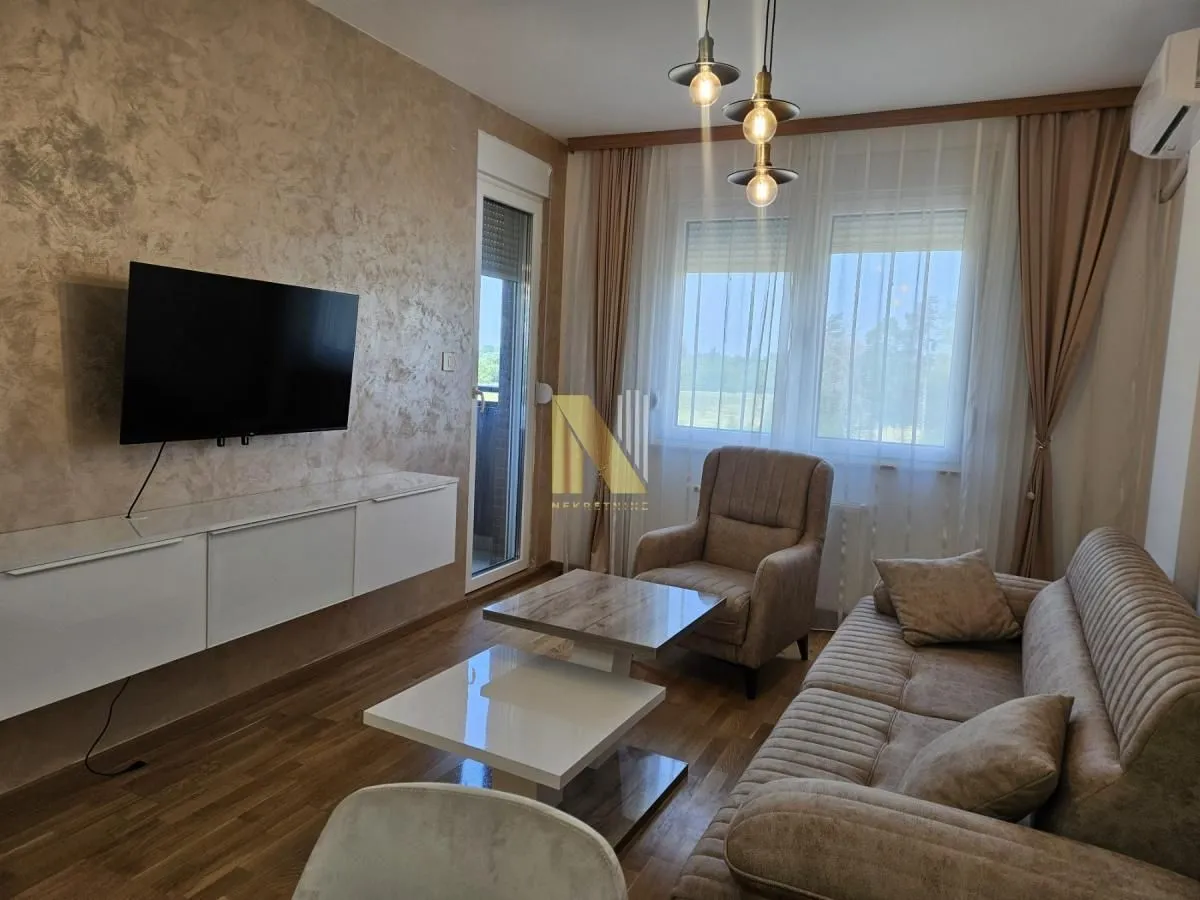 Dnevna soba sa garniturom, stočićem i televizorom na zidu.