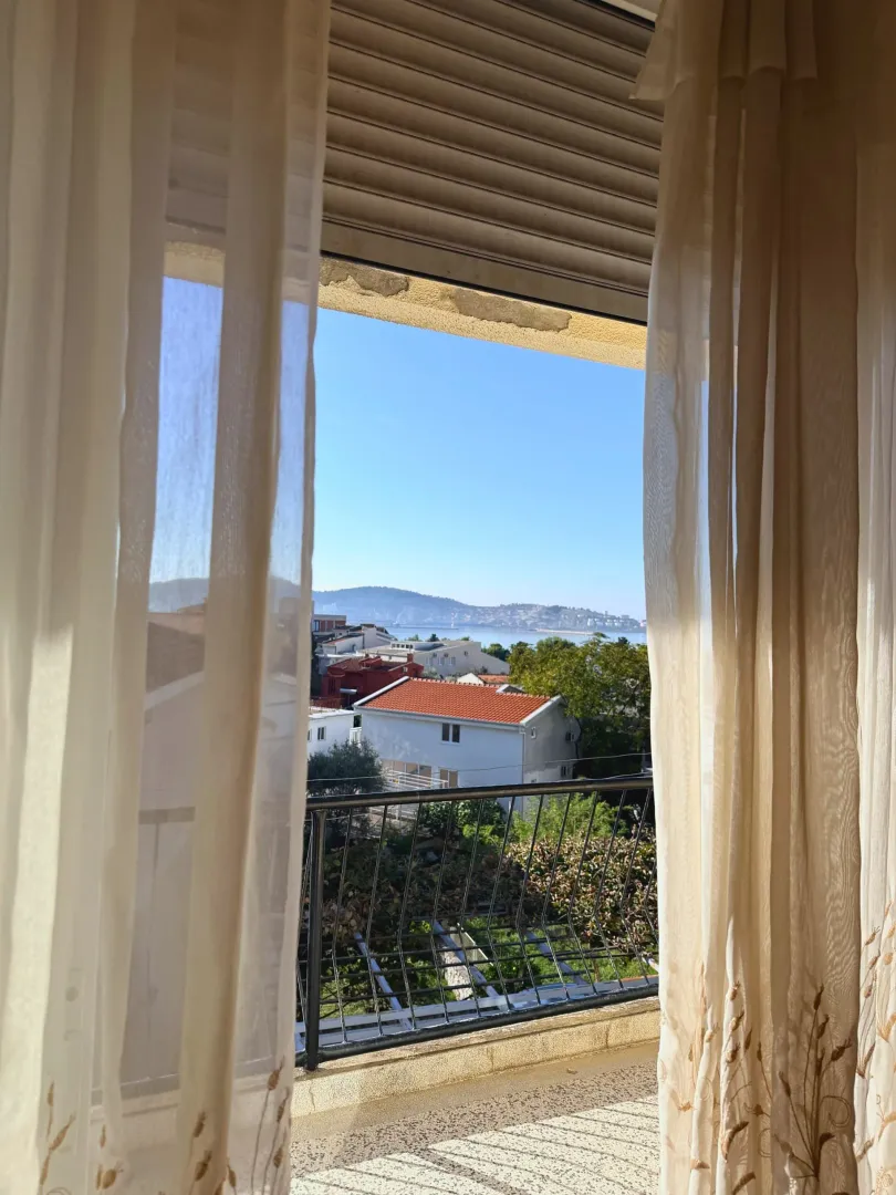 Pogled na okolinu i more kroz prozor sa zavesama.