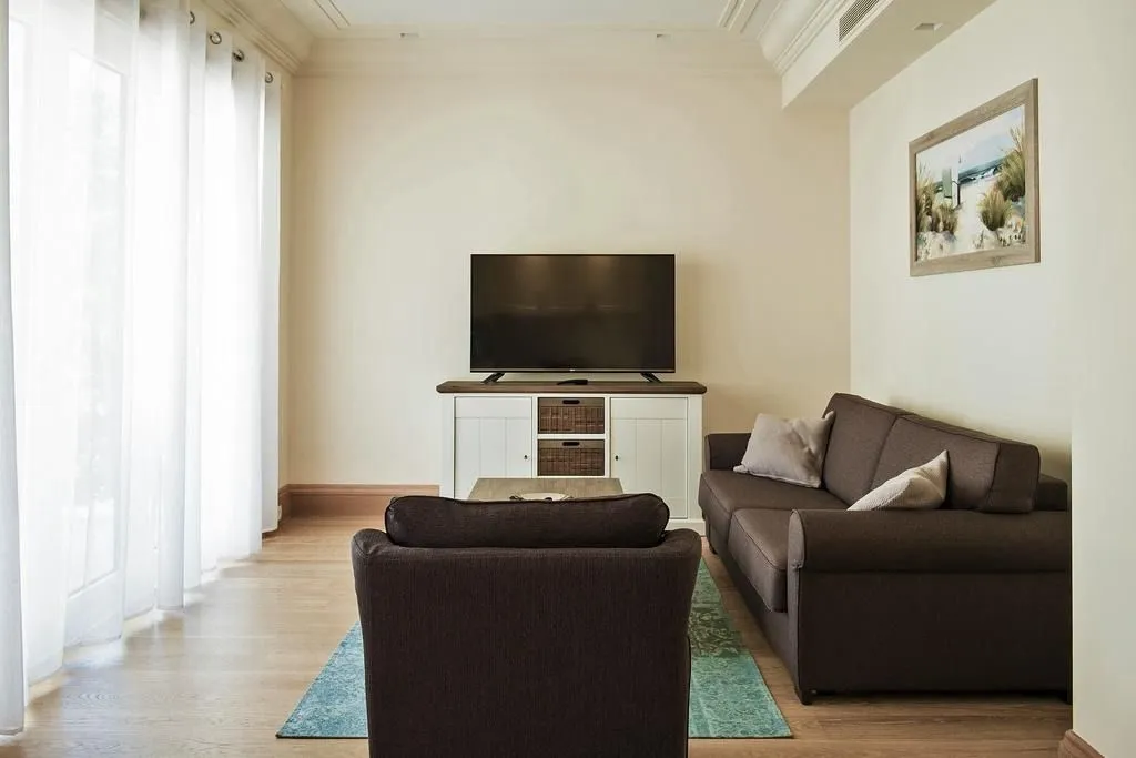 Living room with a sofa set, TV, and a large window with white curtains.