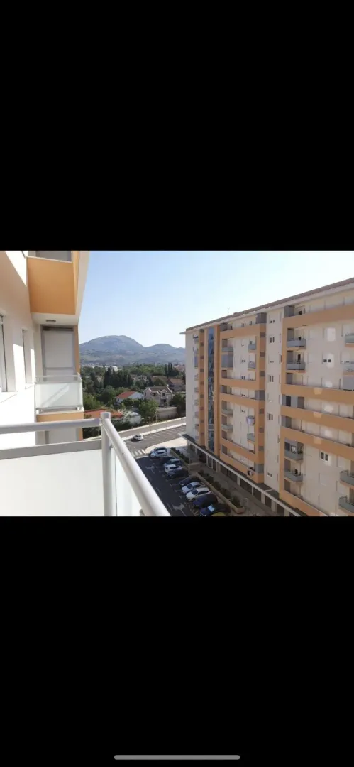 View from the balcony overlooking a neighboring building, parking lot, and mountains.