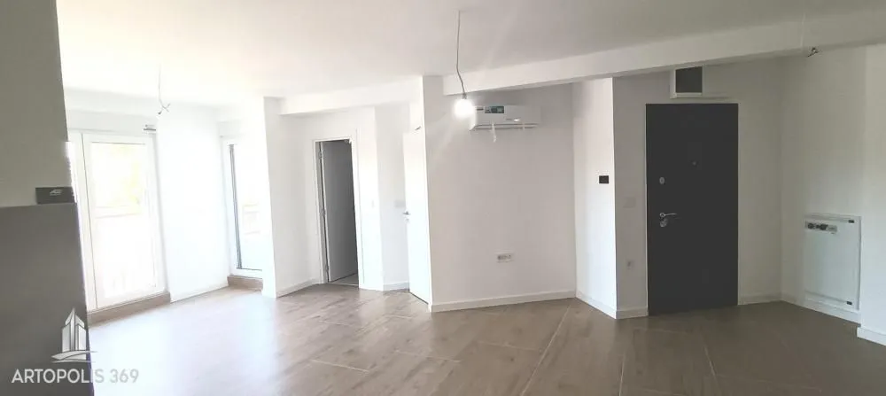 Prazna svetla dnevna soba sa keramičkim podom i ulaznim vratima.