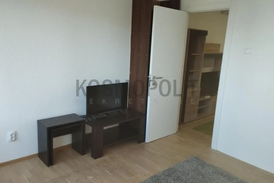 Pogled na deo dnevnog boravka sa TV komodom i otvorenim vratima.