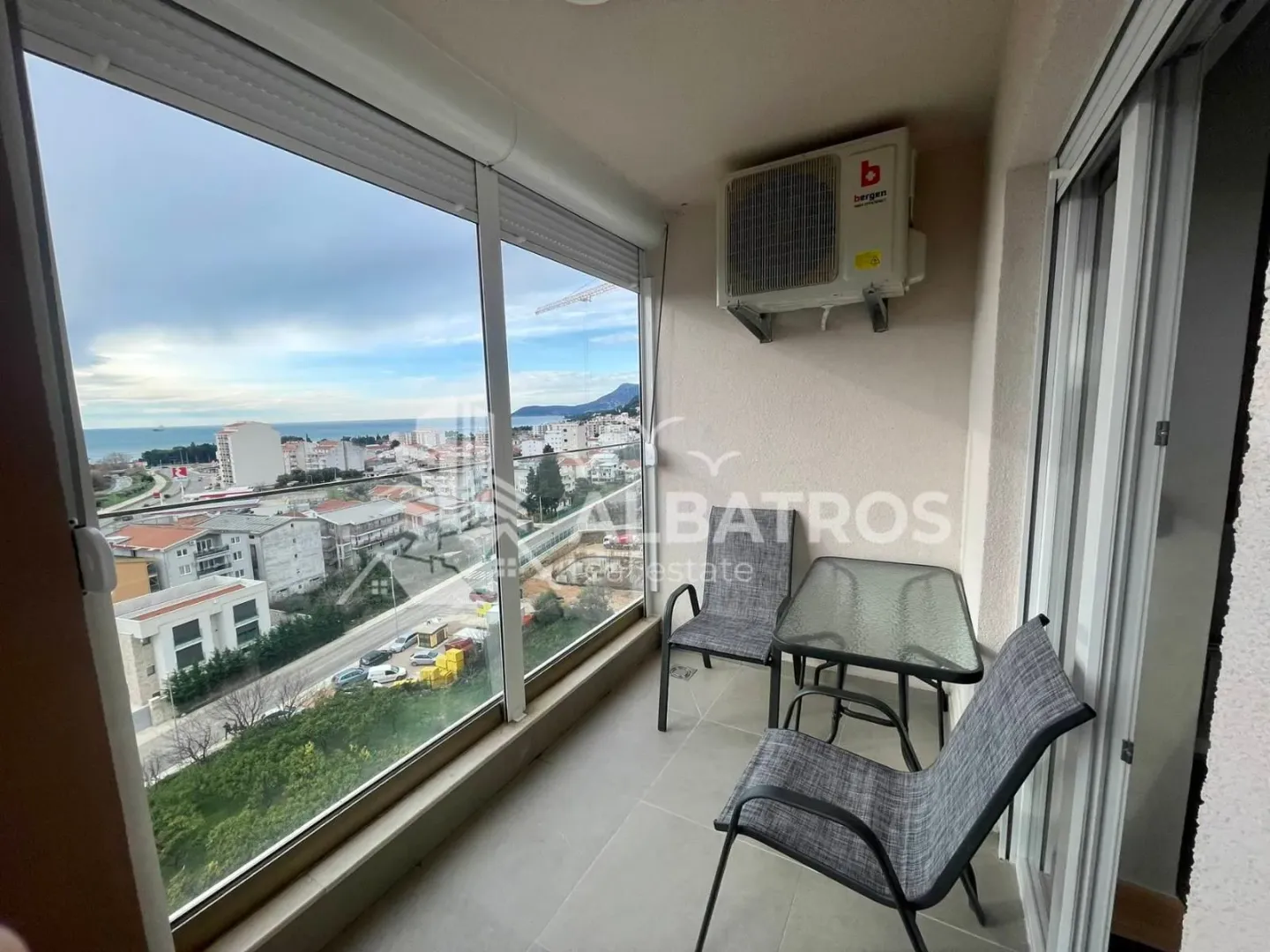 Enclosed balcony with seating furniture and a view of the city and the sea.