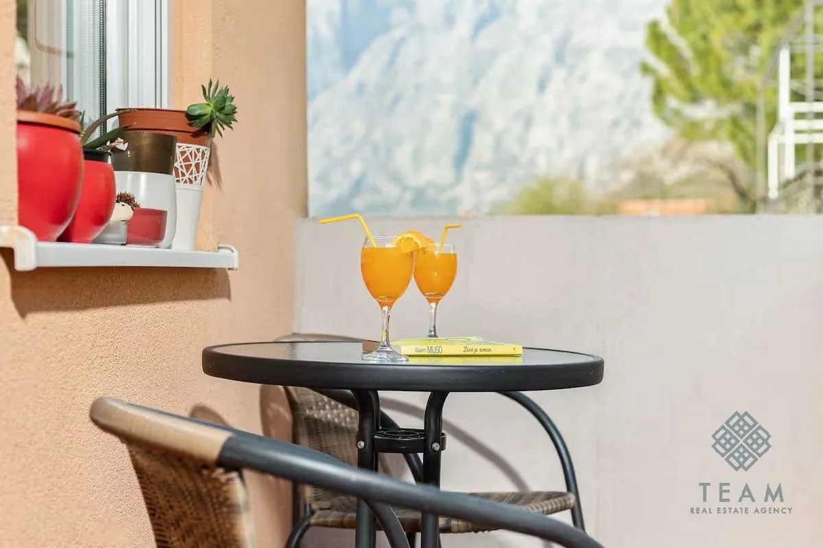 A small table with chairs and glasses of juice on a balcony with a mountain view.