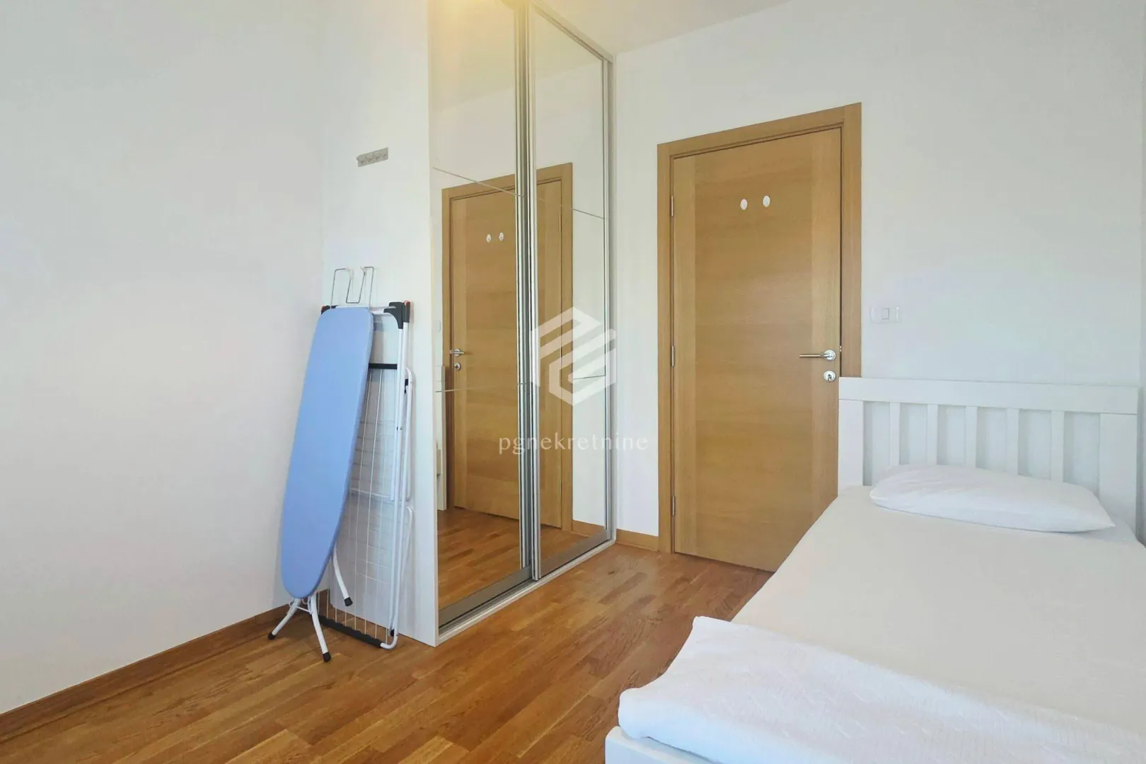 Small bedroom with a bed, wooden flooring, and a built-in mirrored wardrobe.