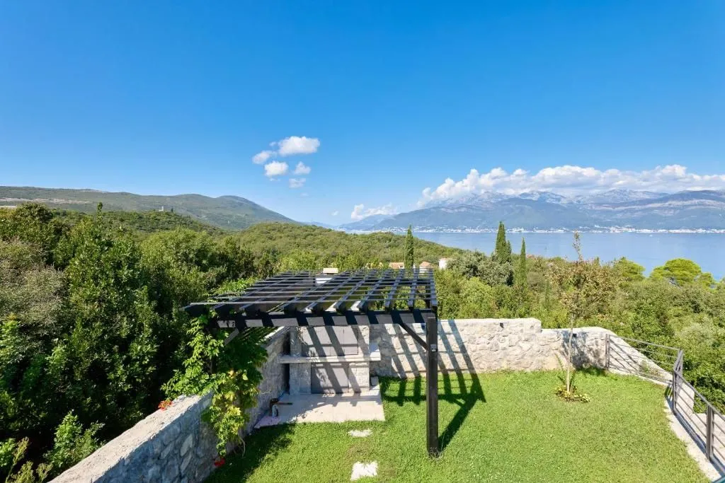 Yard with a stone barbecue, wooden pergola, and sea view.