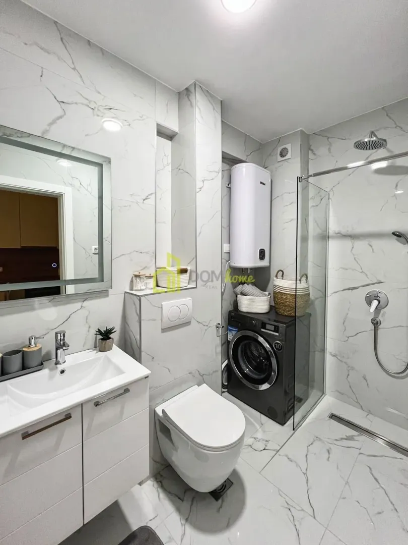 Modernly equipped bathroom with a walk-in shower, washbasin, and washing machine.