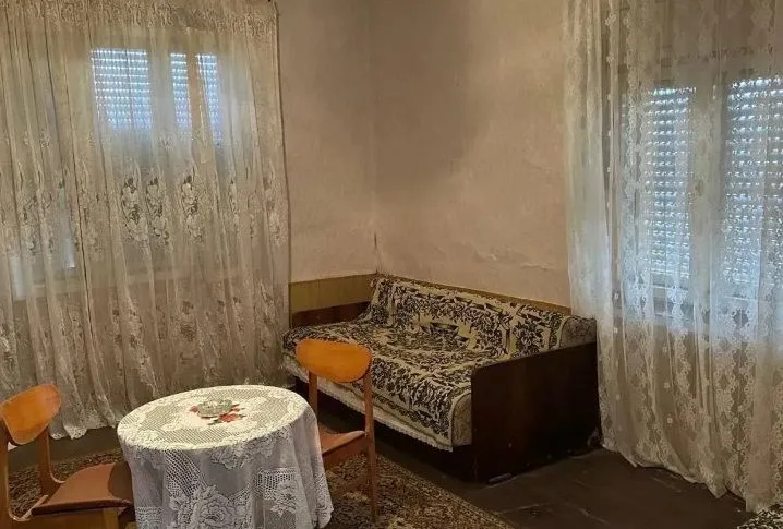 Dnevna soba sa garniturom, stolom i prozorima sa zavesama.