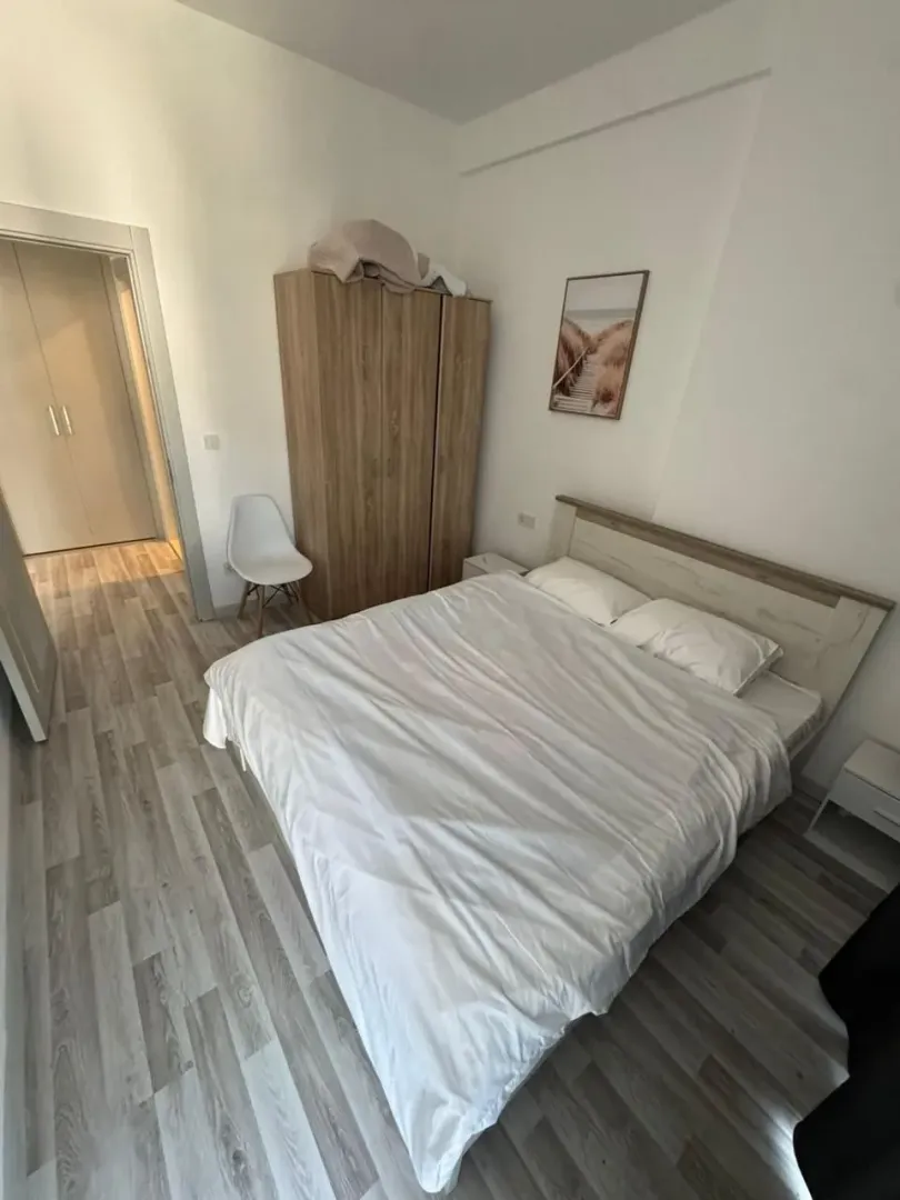 Namještena spavaća soba sa bračnim krevetom, drvenim ormarom i laminatnim podom.