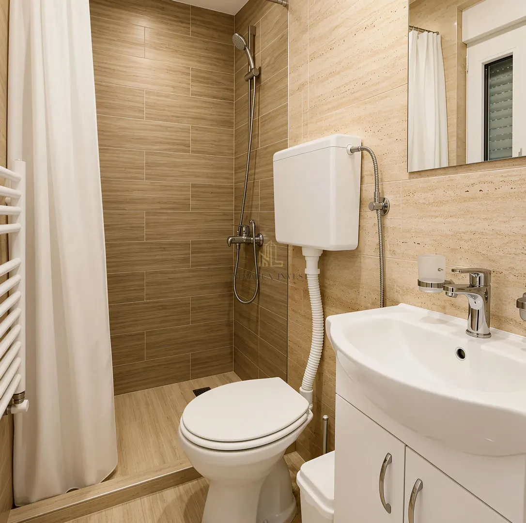 Kompaktno kupatilo sa tuš kabinom, umivaonikom i wc šoljom obloženo keramičkim pločicama u tonovima drveta.