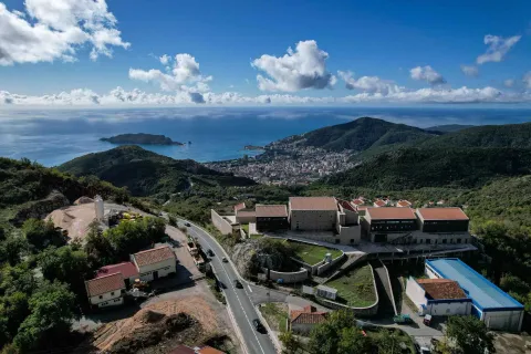 Pogled iz vazduha na kompleks zgrada sa okolnim pejzažom i morem u pozadini. - image 5