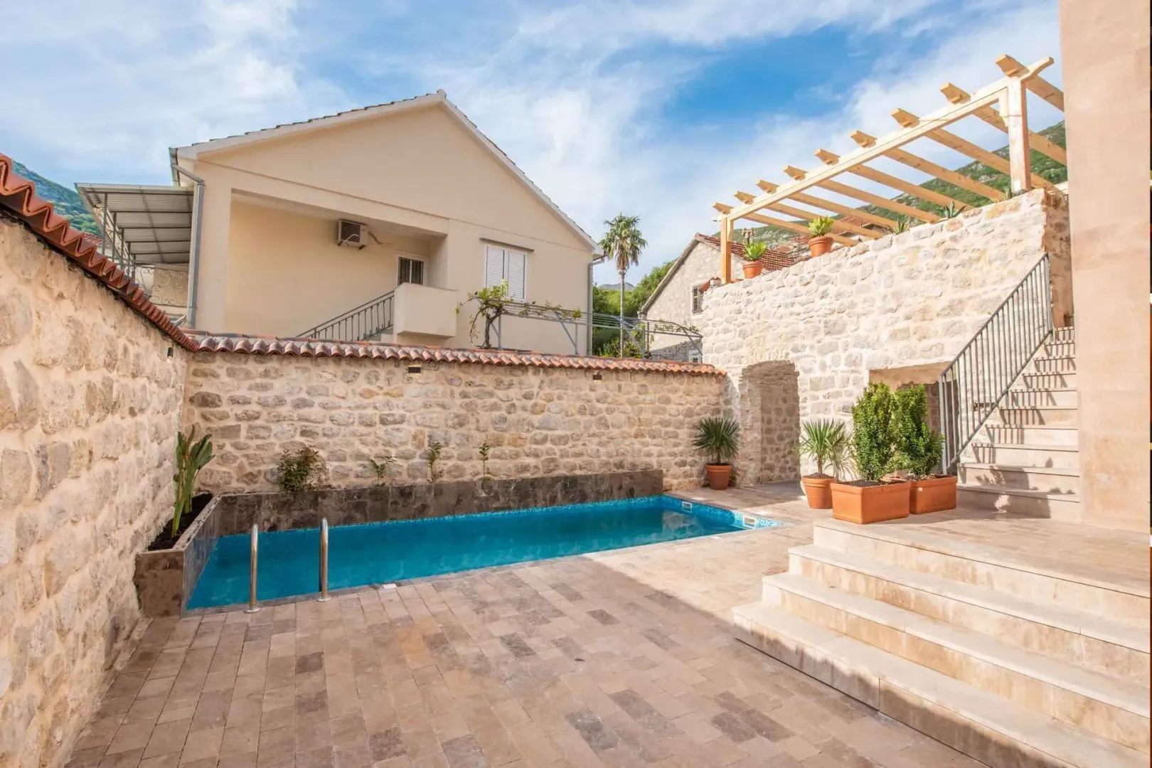 Courtyard of the house with a swimming pool, paved patio, and stone walls.