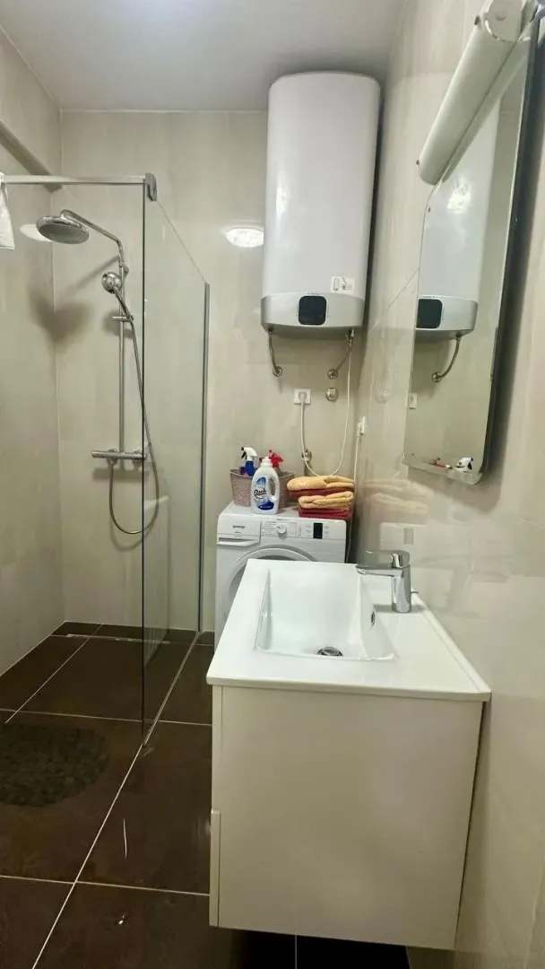 Moderno opremljeno kupatilo sa tuš kabinom, umivaonikom i veš mašinom.
