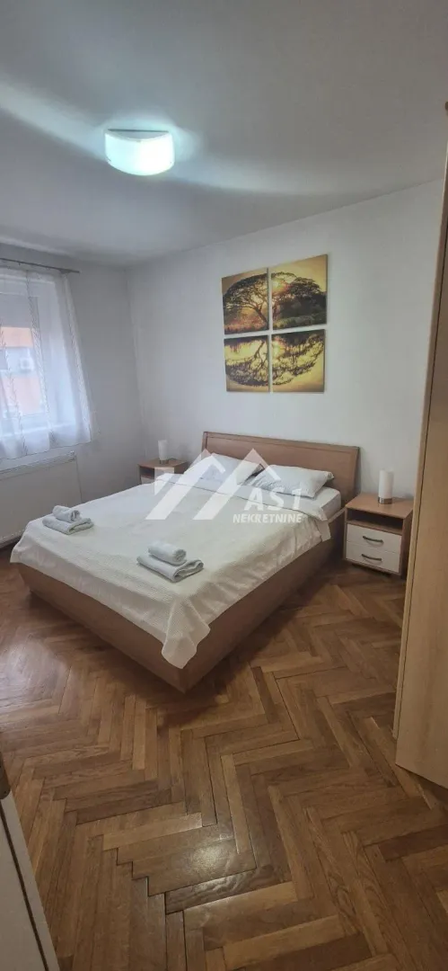 Spavaća soba sa bračnim krevetom, noćnim stočićima i drvenim podom.