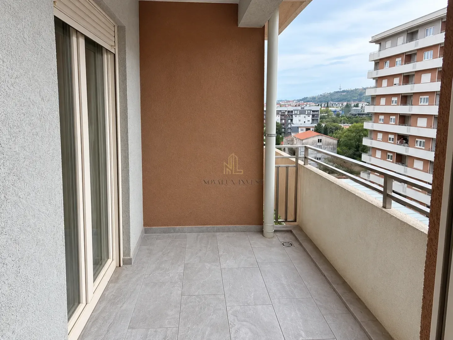 Nenamješten balkon sa pločicama na podu i pogledom na okolne zgrade.