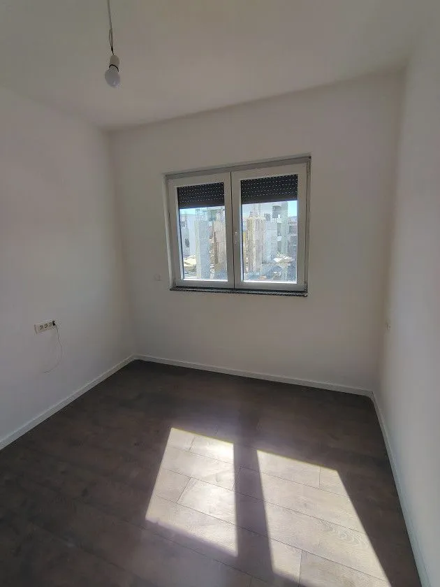 Prazna soba sa tamnim laminatom i prozorom.
