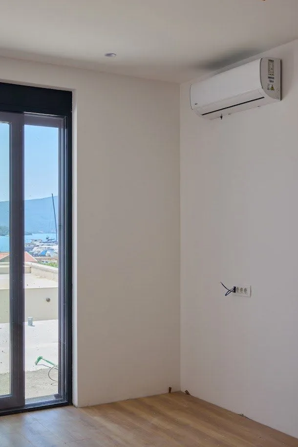 Unutrašnjost sobe sa klima-uređajem i pogledom na more kroz balkonska vrata.