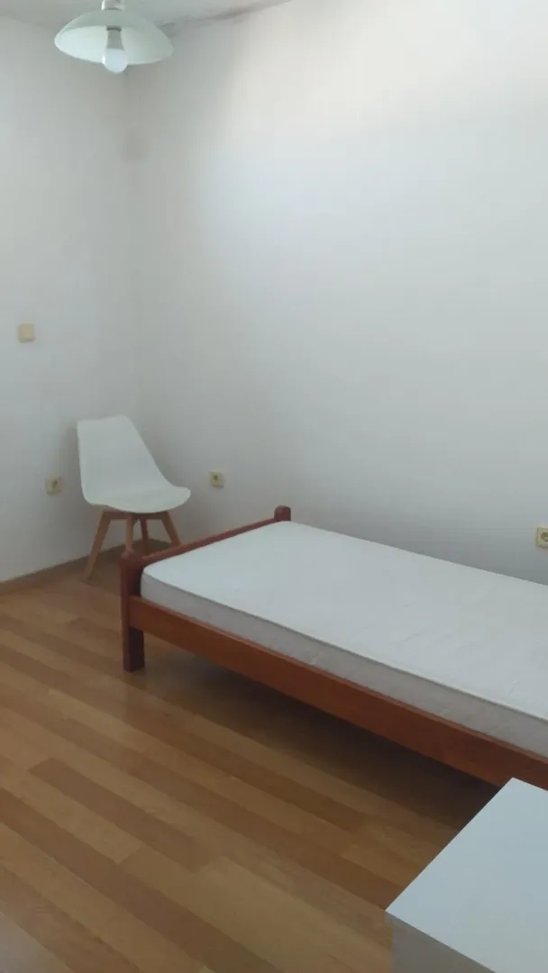 Jednostavna spavaća soba sa jednim krevetom i stolicom.