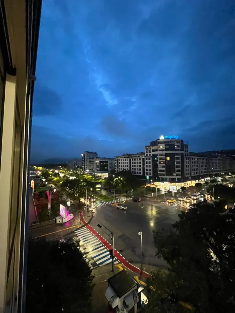 Pogled sa prozora na osvijetljene gradske ulice i zgrade u sumrak.