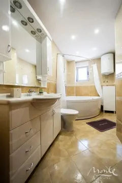 Kupatilo opremljeno umivaonikom sa ormarićem, kadom i toaletom. - image 5