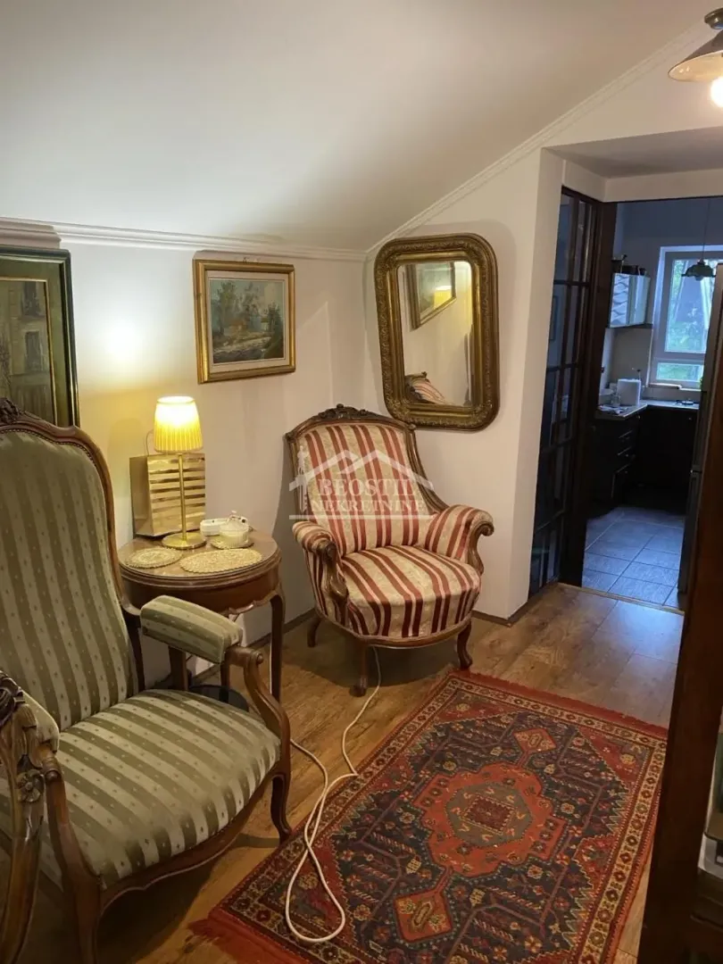 Tradicionalno opremljen dnevni boravak sa foteljama, tepihom i pogledom na kuhinju.