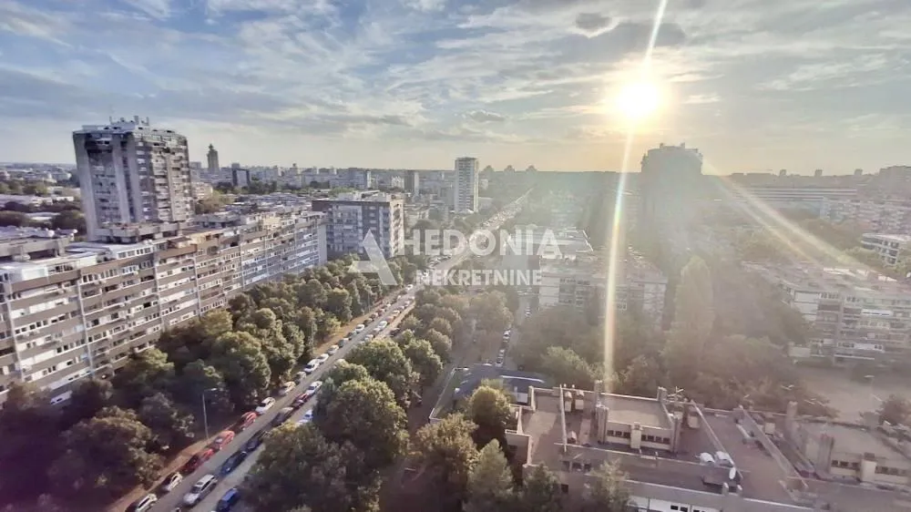 Pogled iz visine na gradski pejzaž i bulevar sa parkiranim automobilima.
