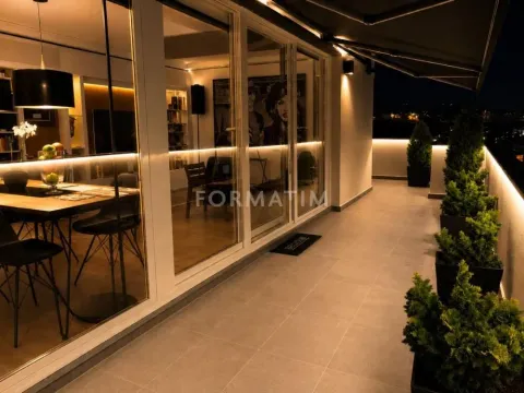 Osvetljena terasa sa drvećem u saksijama i pogledom na enterijer stanova noću. - image 15