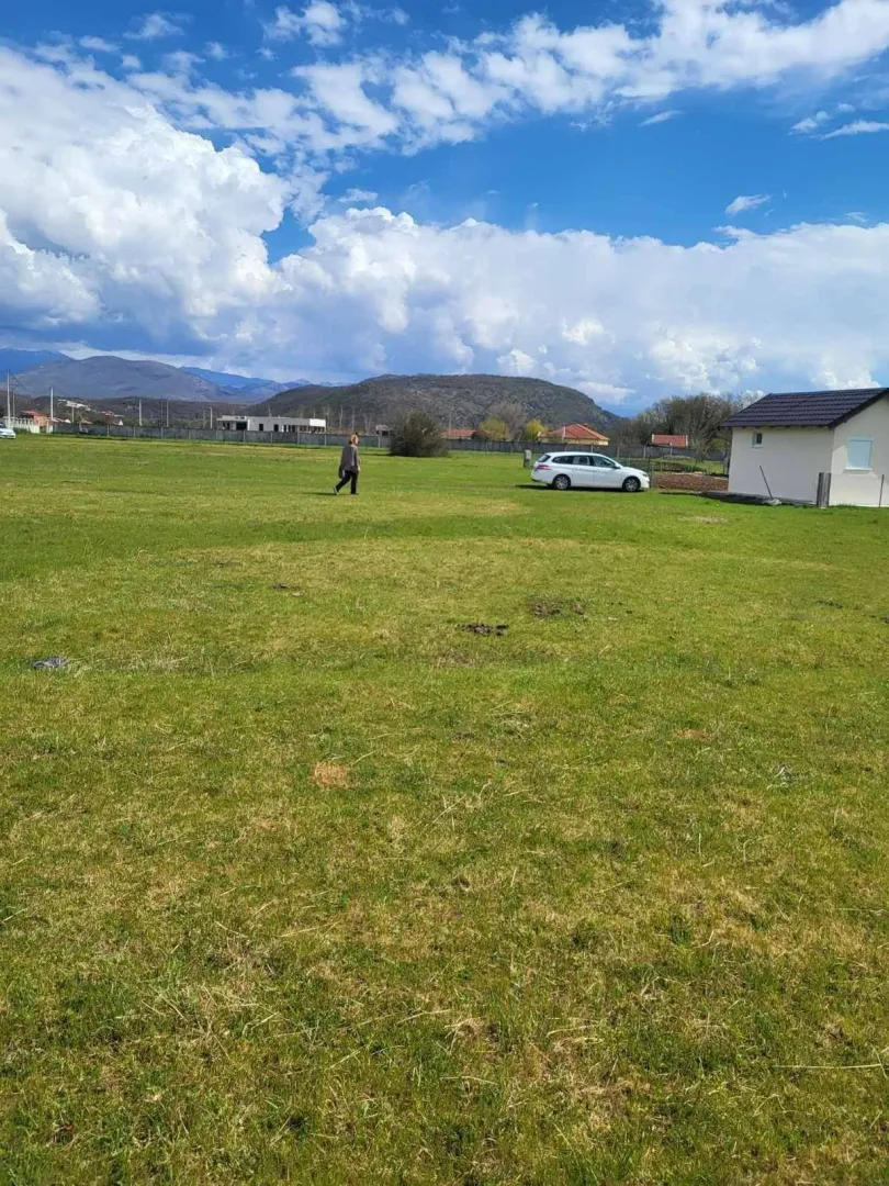 Prostran zeleni plac sa pomoćnim objektom u prirodnom okruženju.