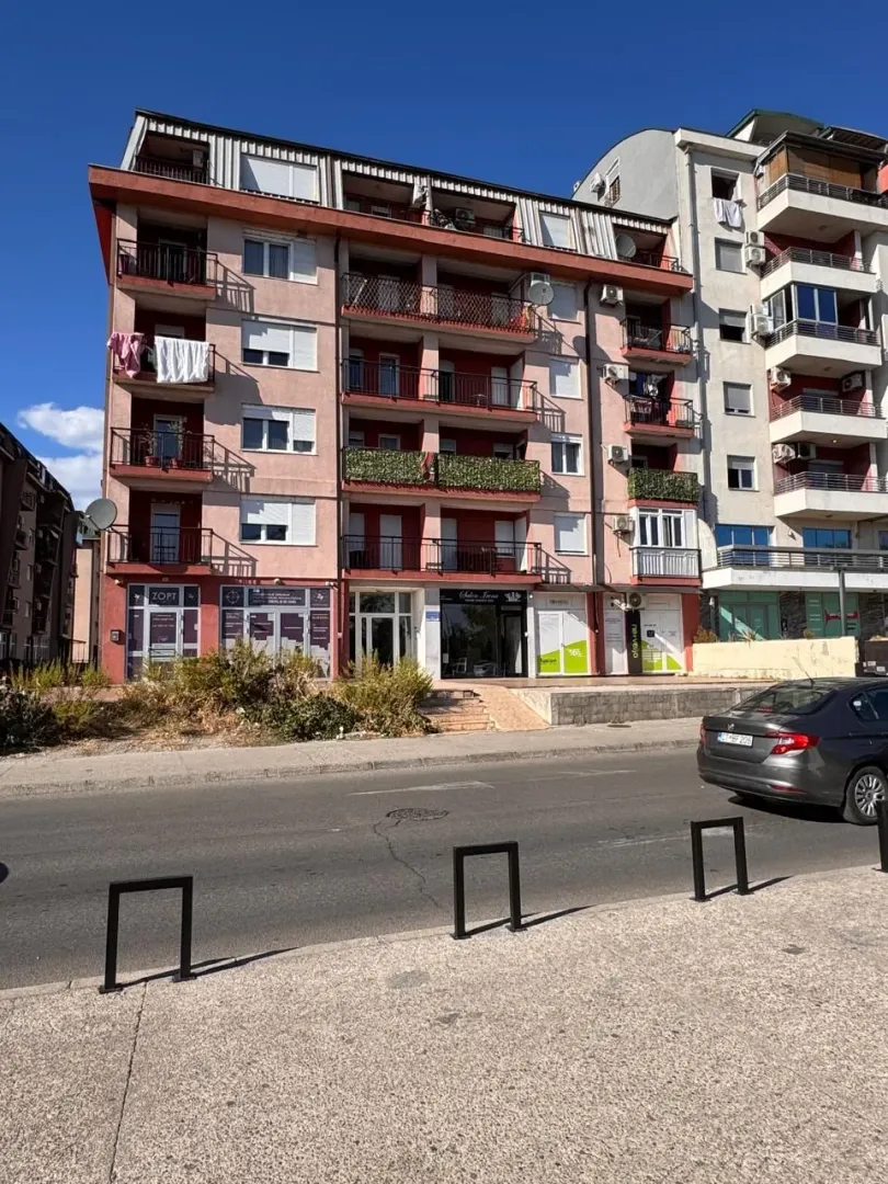 Pogled na spoljašnjost stambene zgrade sa ulicom u prvom planu.