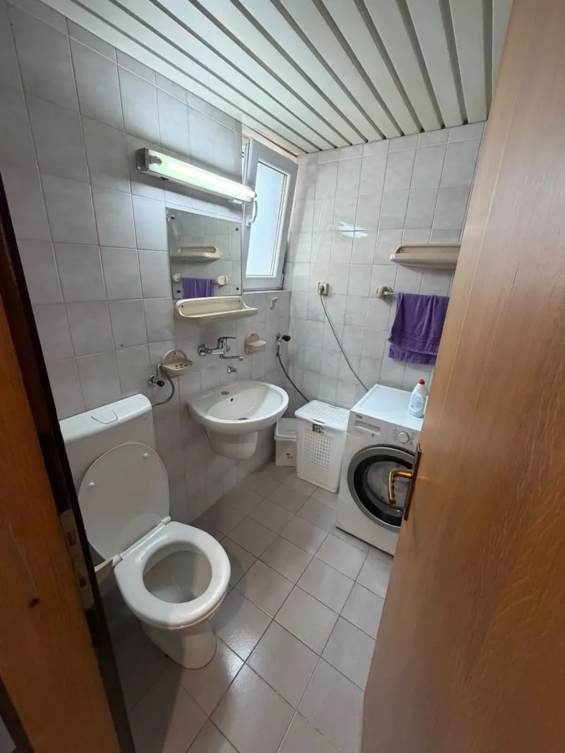 Manje kupatilo sa sanitarijama, umivaonikom, tuš kabinom i mašinom za veš.
