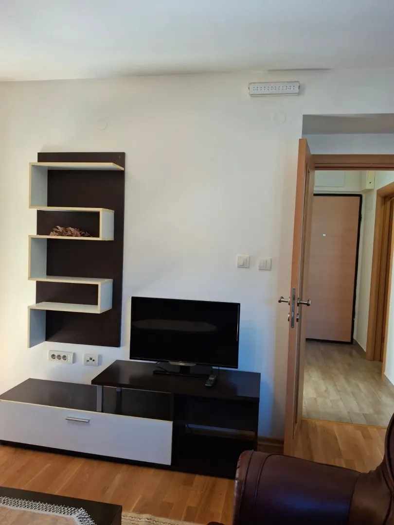 Dnevna soba sa TV komodom i policama na zidu.