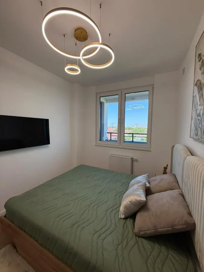 Spavaća soba sa bračnim krevetom, TV-om i modernim lusterom.