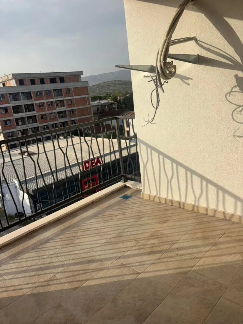 Nenamješten balkonski prostor sa keramičkim pločicama i pogledom na okolne zgrade.