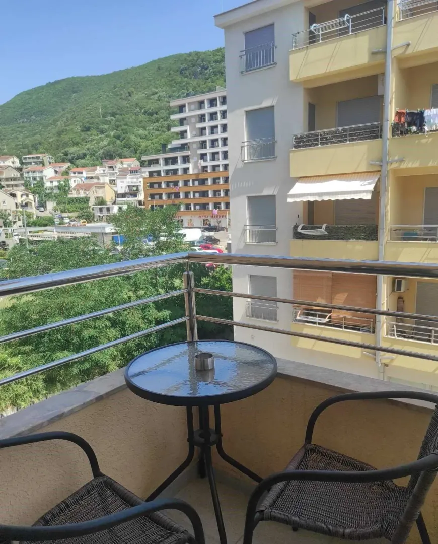 Furnished balcony with a table and chairs and a view of surrounding buildings and hills.