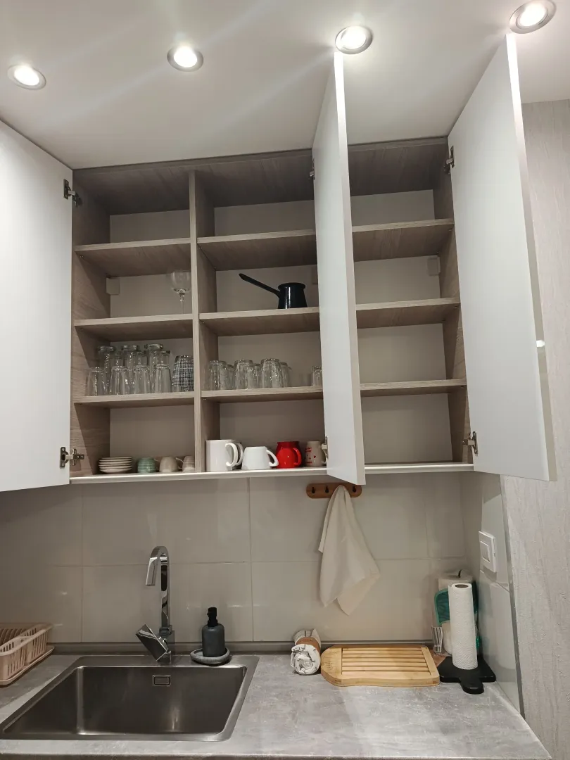 Kitchen sink and an open wall cabinet with glasses and mugs.