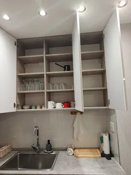Kitchen sink and an open wall cabinet with glasses and mugs. - image 16