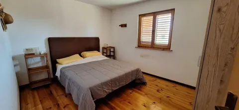 Spavaća soba sa bračnim krevetom, drvenim podom i prozorom sa kapcima. - image 11
