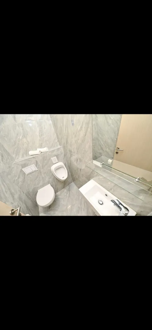 Modern bathroom equipped with grey ceramic tiles, toilet, urinal, and washbasin.