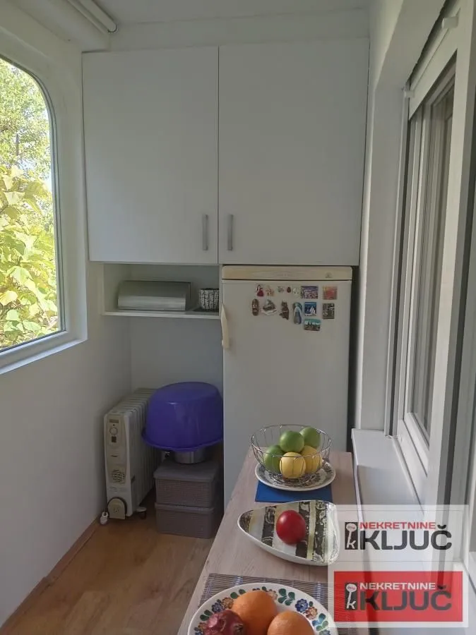 Manja kuhinja sa belim elementima, frižiderom i prozorom.