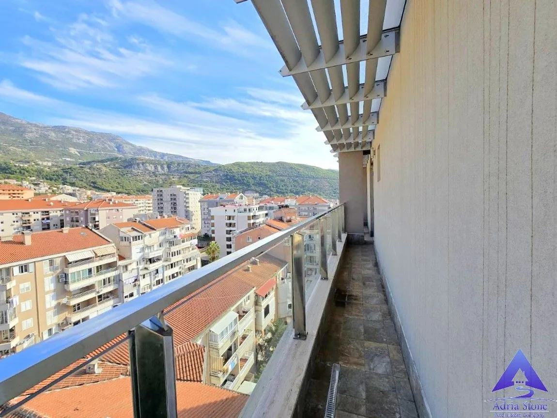 Dugačak natkriveni balkon sa staklenom ogradom i pogledom na grad i planine.