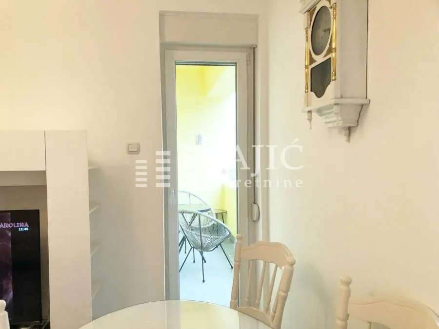 View from the living room towards the balcony with a dining table and a wall clock.