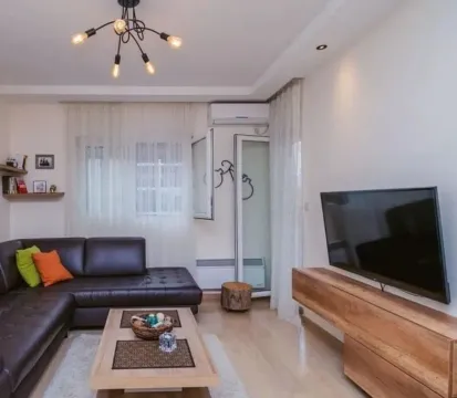 Living room with a dark sectional sofa, wooden coffee table, and television. - image 2