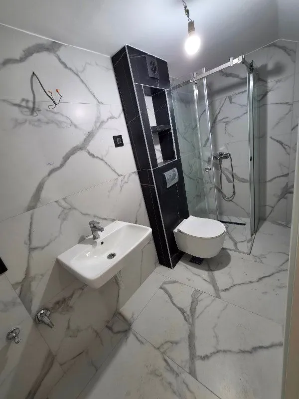 Kupatilo opremljeno umivaonikom, WC šoljom i tuš kabinom sa mermernim pločicama.