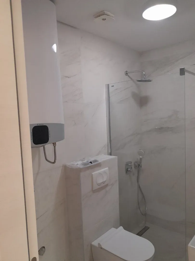 Bright bathroom featuring a walk-in shower, toilet, and water heater.