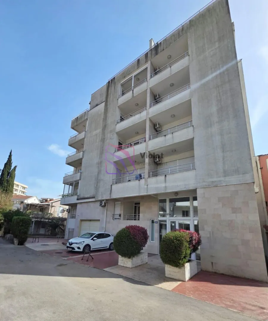 Exterior view of the residential building with balconies and parking in front of the entrance.