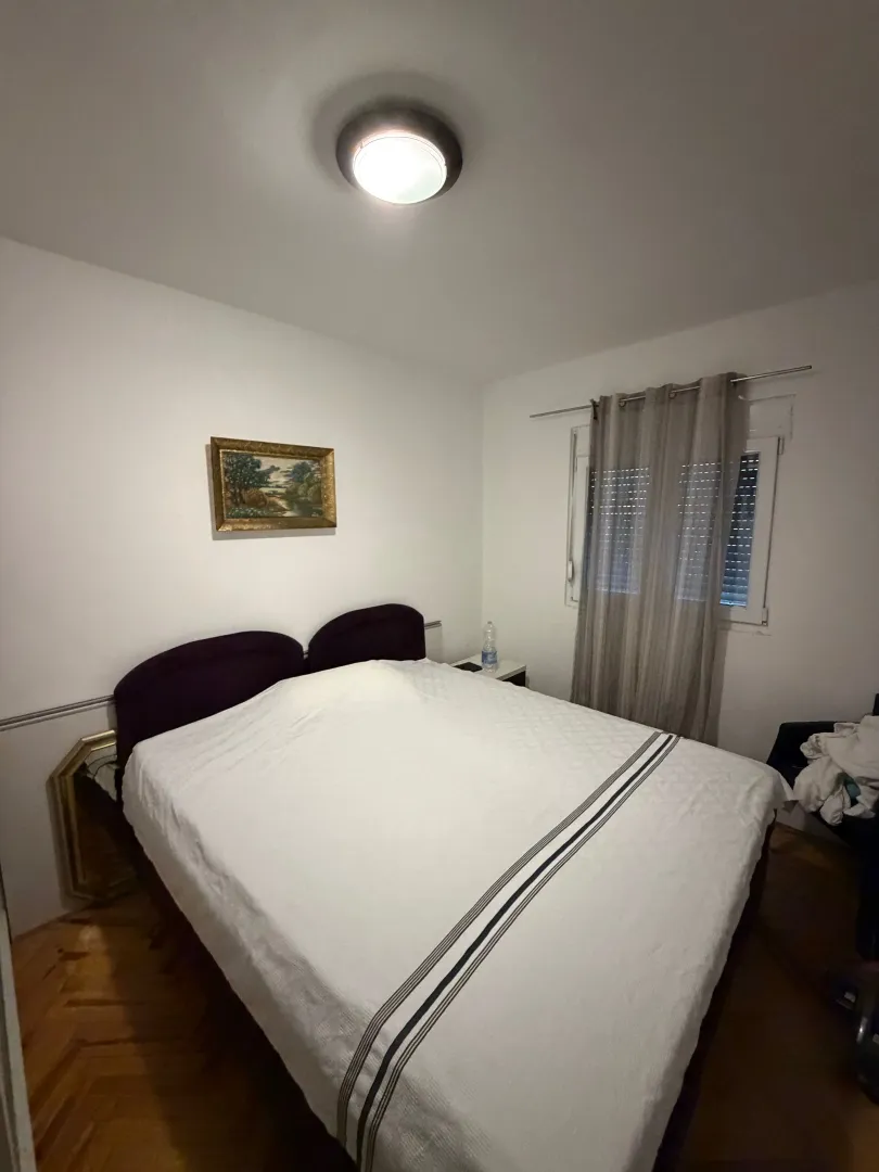 Spavaća soba sa bračnim krevetom, prozorom i umjetničkom slikom na zidu.