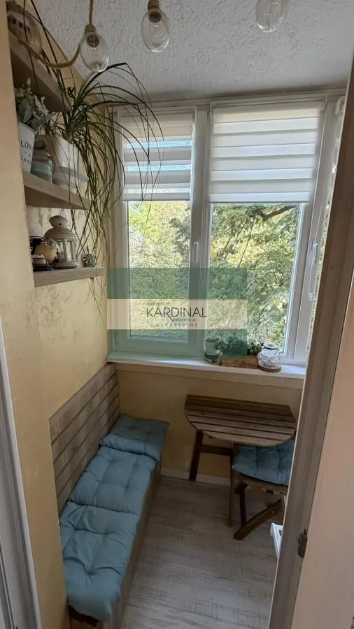 Zastakljeni balkon sa klupom, drvenim stočićem i pogledom na zelenilo.